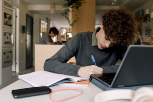 Teenage boy with brown curly hair doing homework while sitting at table