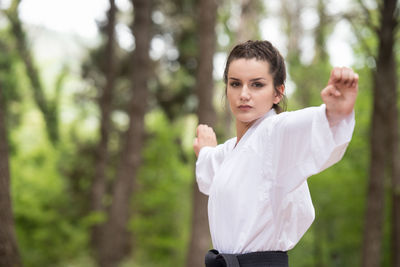 Portrait of young woman standing against trees