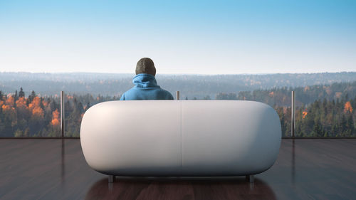 Rear view of man sitting on sofa against landscape and clear sky