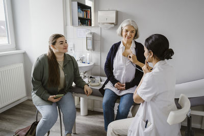 Doctor listening heartbeat of senior woman sitting with daughter in clinic