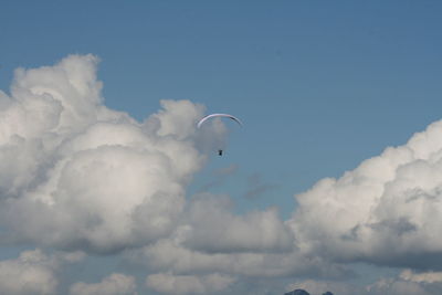 Low angle view of people paragliding against blue sky