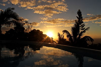 Silhouette trees reflection in infinity pool against sky during sunset