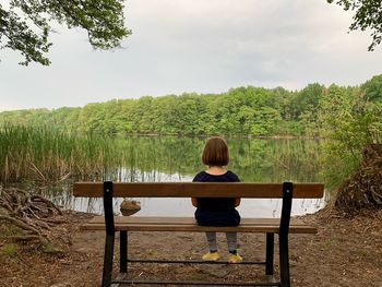 Rear view of woman sitting by lake against sky