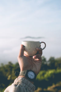 Midsection of man holding coffee cub against sky