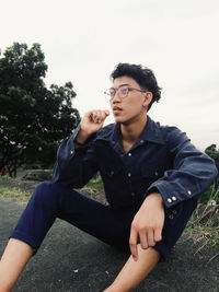 Young man sitting on roadside against sky