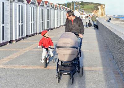 Father with a stroller and daughter on a bicycle are walking together on the beach