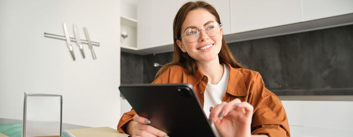 Portrait of young woman using digital tablet while sitting on table