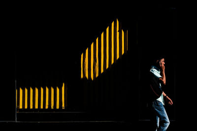 Side view of man standing against illuminated wall at night
