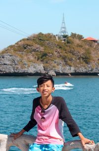 Portrait of smiling woman sitting by sea against sky