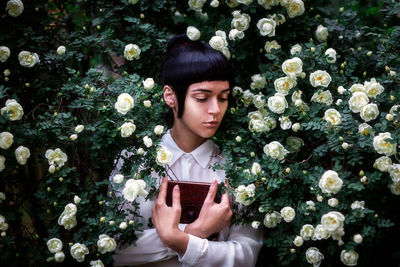 Close-up of young woman holding book by flowers at park