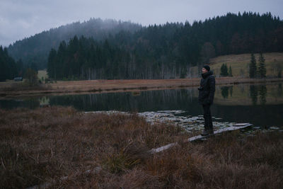 Man standing on shore by lake against trees