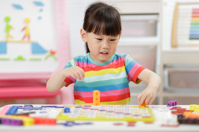 Cute girl playing with building blocks at classroom