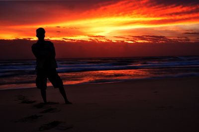 Silhouette of man standing on beach against sunset sky