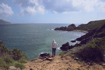 Rear view of man standing on rock by sea against sky