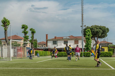 People playing soccer on field against buildings