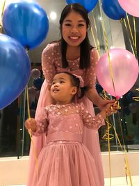 Low angle portrait of mother with daughter amidst balloons during birthday