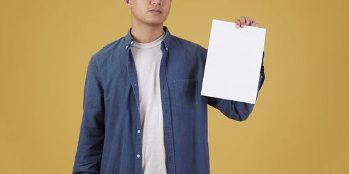 Midsection of man holding paper while standing against yellow background