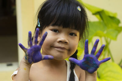 Front view of a little asian girl smiling and looking to a camera with her watercolor painted hand.