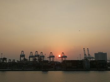 Cranes at commercial dock against sky during sunset