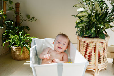 Little baby bathing in brightly lit room among flowers showing his bare feet