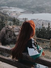 Rear view of woman looking at view of cityscape while sitting on bench