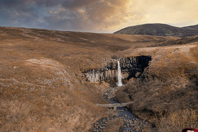 Beautiful svartifoss waterfall amidst basalt rocky cliffs against sky at sunset