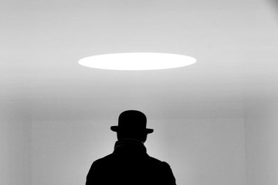 Rear view of man wearing hat standing in illuminated room