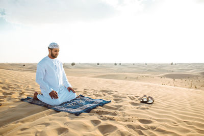 Man praying while sitting on sand in desert