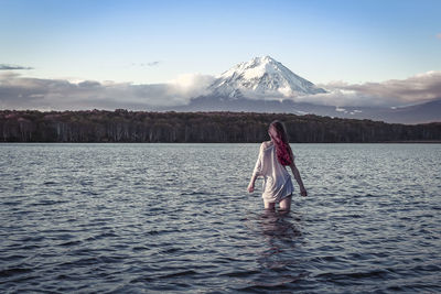 Rear view of woman standing in lake against snowcapped mountains