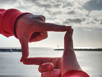 Fingers picture frame on sunrise seaside. sunlight on beach. female hand gesture in love concept