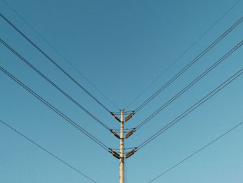 Low angle view of electricity pylon against clear blue sky