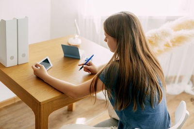 Rear view of woman writing in book at table