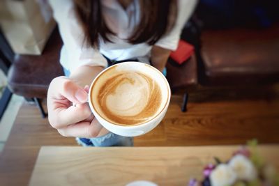 Cropped image of woman holding cappuccino at cafe