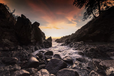 Rocks on beach against sky during sunset