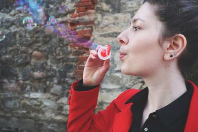 Close-up of young woman blowing bubbles against wall