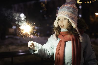 Portrait of young woman holding sparkler at night