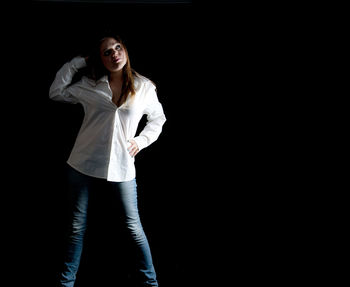 Portrait of young woman standing against black background