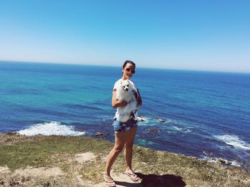 Young woman standing with pomeranian on cliff against sea