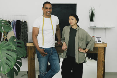 Portrait of smiling male tailor standing with female sales staff near table at store