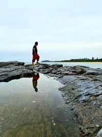 Full length of man standing on rock at beach against sky
