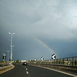 Rainbow over road in city against sky