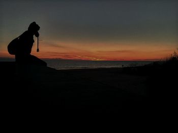 Silhouette woman photographing sea against sky during sunset