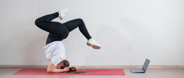 Full length of woman doing headstand against wall at home