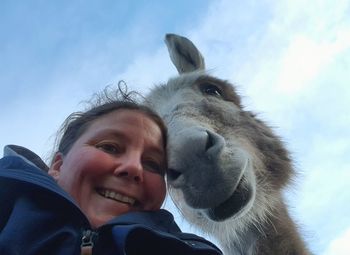 Portrait of smiling young woman with donkey against sky 