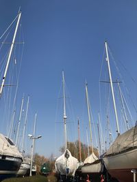 Low angle view of sailboats moored at harbor against clear blue sky