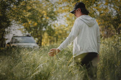 Side view of young man walking on field  by the car