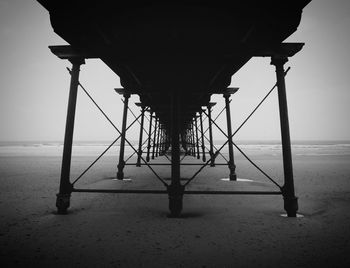 Silhouette of pier on beach against clear sky