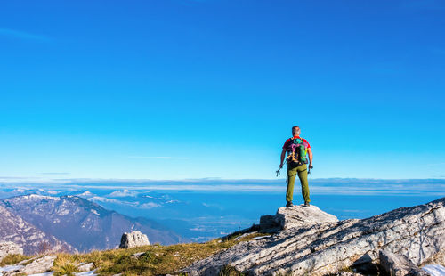 Rear view of man standing on mountain against blue sky