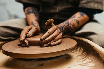 Closeup of dirty hands of anonymous craftsman using pottery wheel and making clay pot in workshop