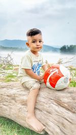 Portrait of boy sitting by lake against sky